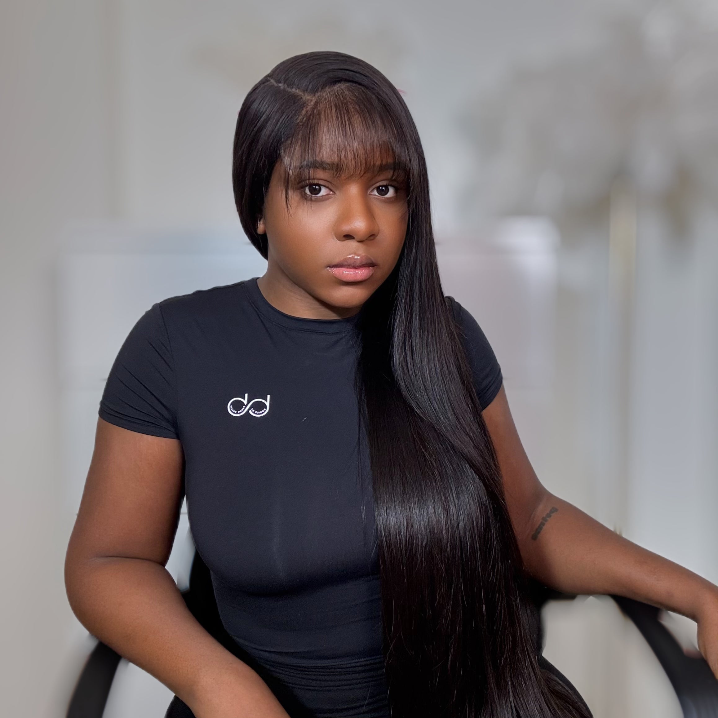 Person wearing a black t-shirt with a logo, sitting against a neutral background