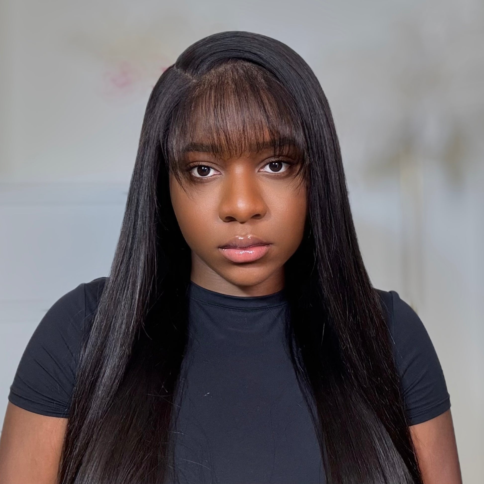 Person with long straight hair wearing a black shirt against a neutral background