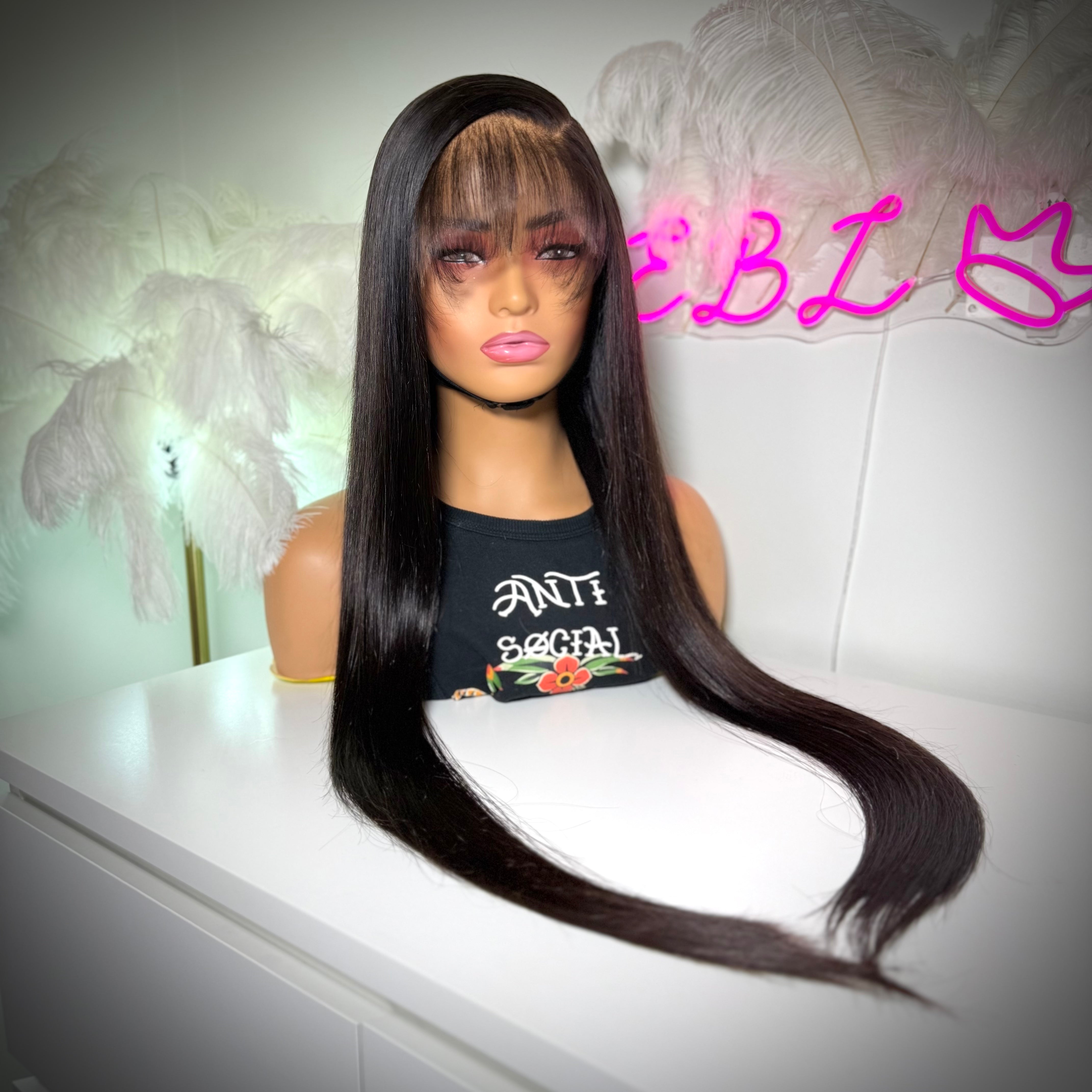 Mannequin head with long black wig on a white surface, with 'EBL' text in the background.