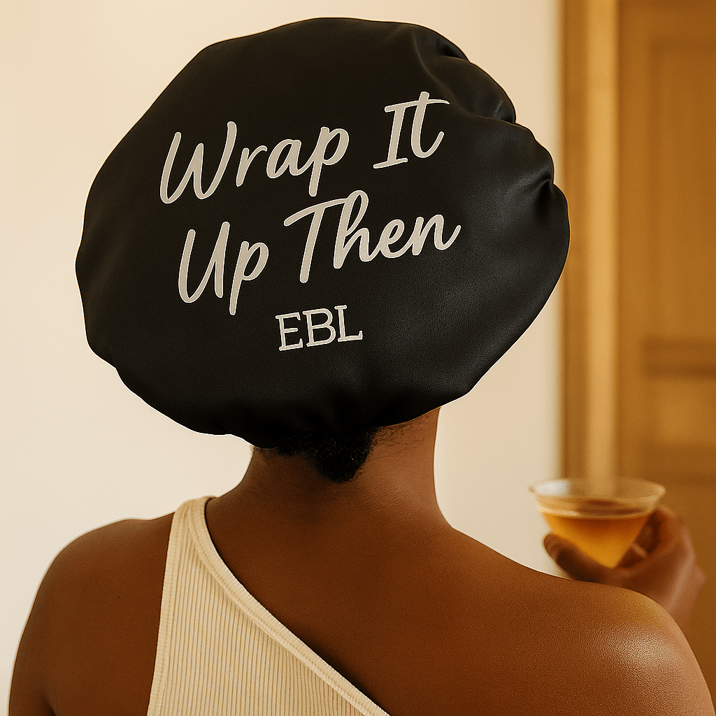 Person wearing a black satin bonnet with 'Wrap It Up Then EBL' text, holding a glass of orange juice.