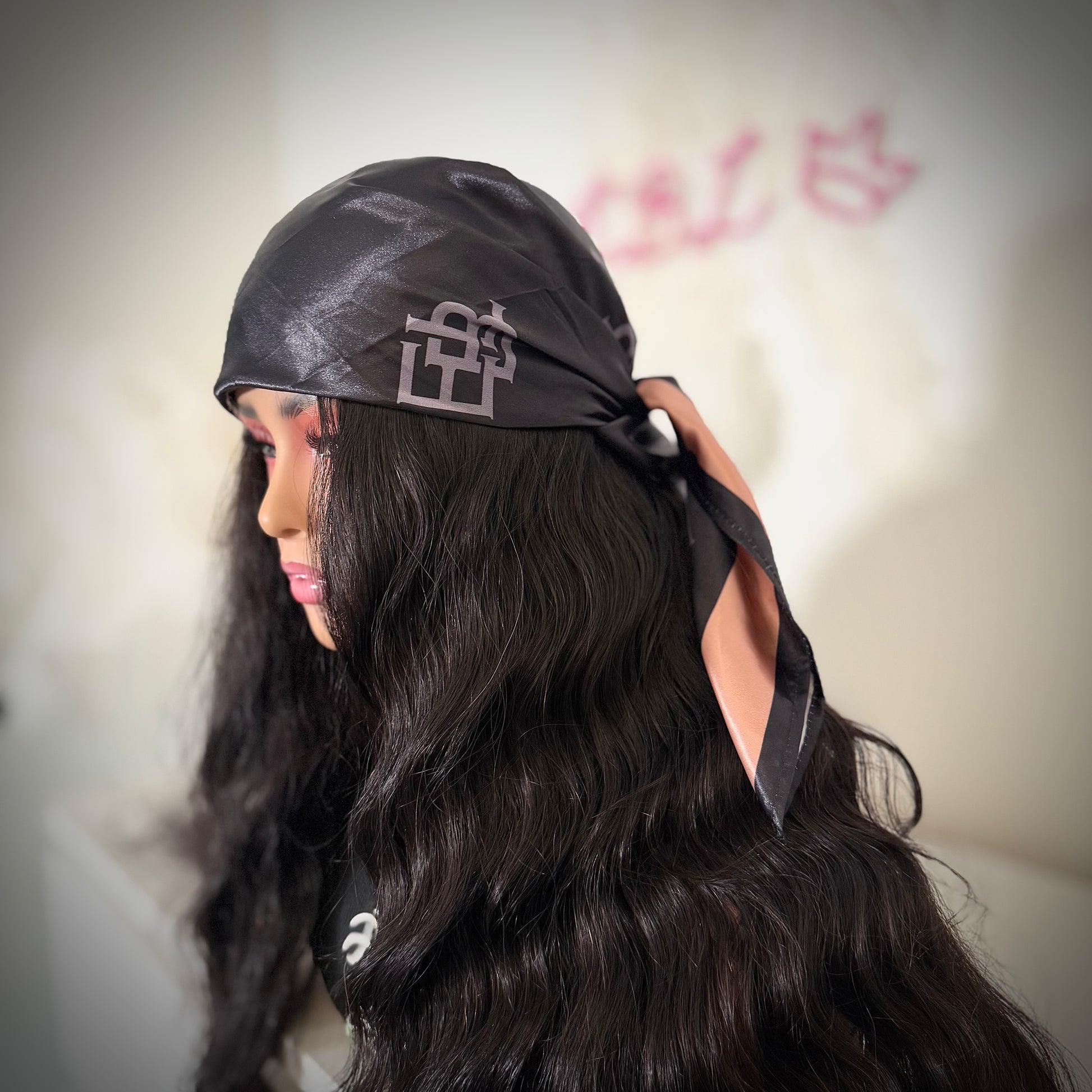 Person wearing a black headscarf with a logo, against a blurred background.