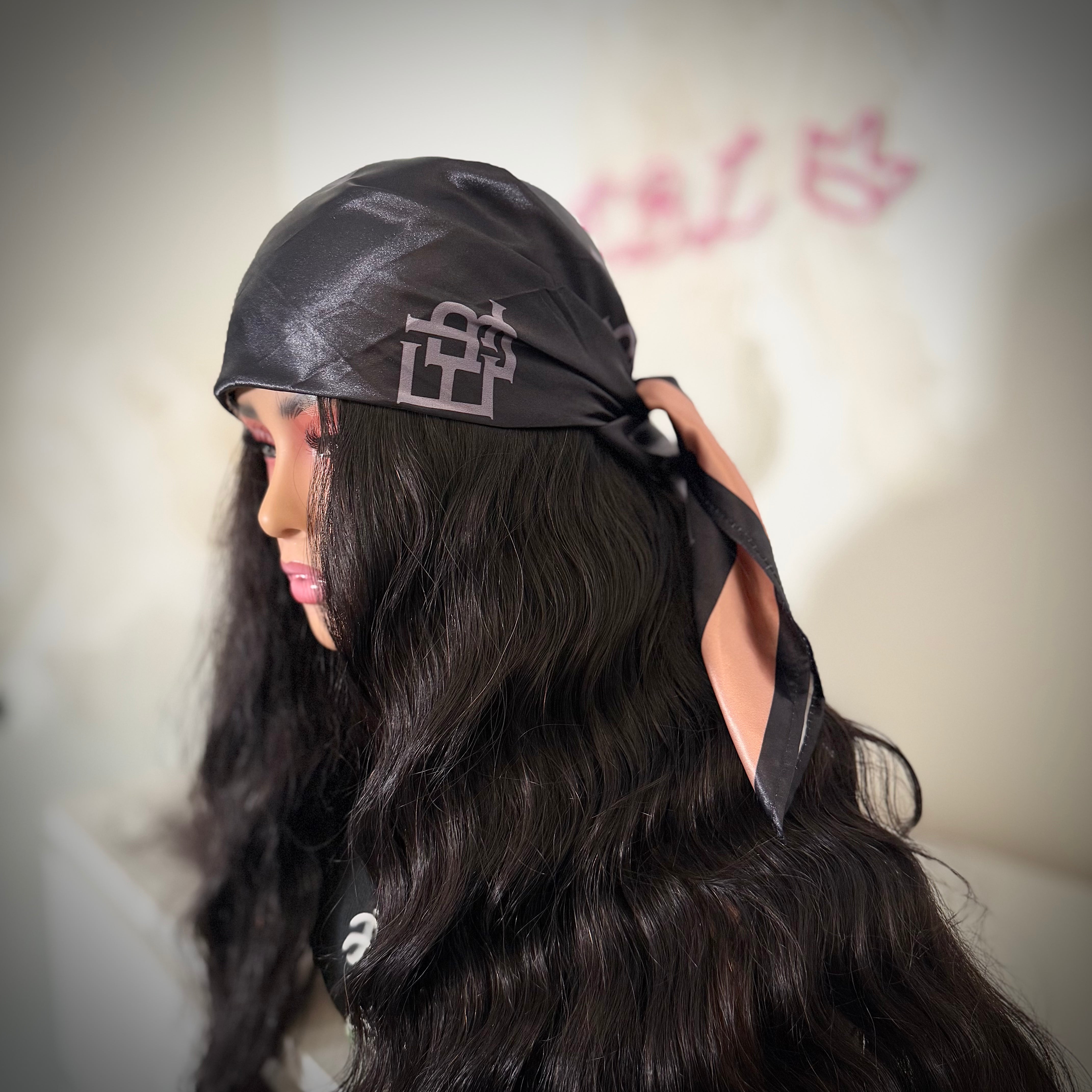 Person wearing a black headscarf with a logo, against a blurred background.